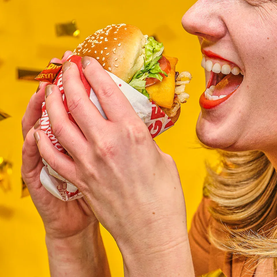 Woman smiling as she lifts a Red Robin burger against a yellow background