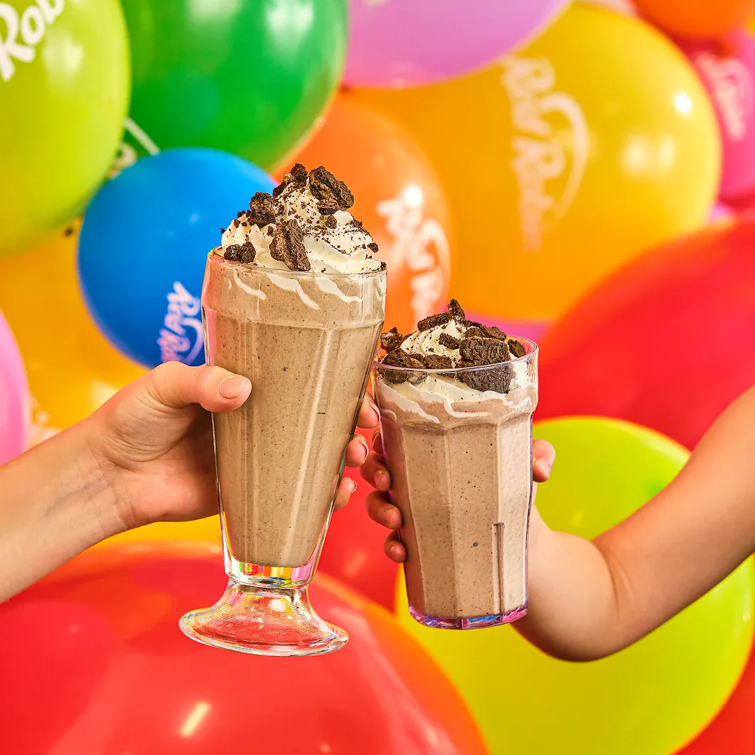 Two Red Robin milkshakes held in front of colorful balloons